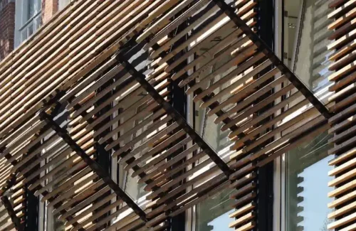 Mit Holzleisten verkleidete Fassade mit klappbaren Leistenelementen vor Holzfenstern